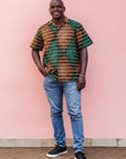 The model is wearing brown, camel, green and black diamond shaped geometric print shirt