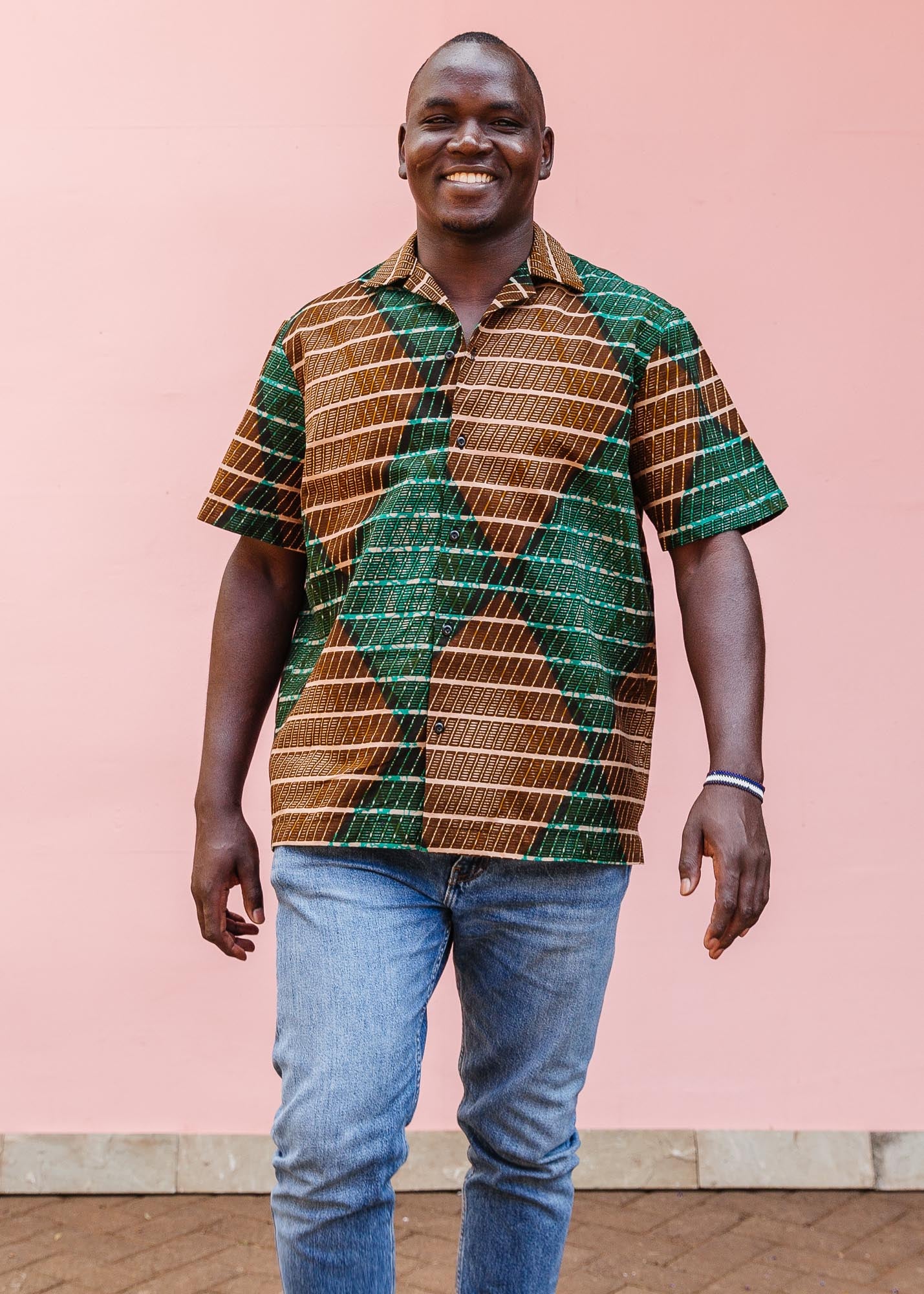 The model is wearing brown, camel, green and black diamond shaped geometric print shirt