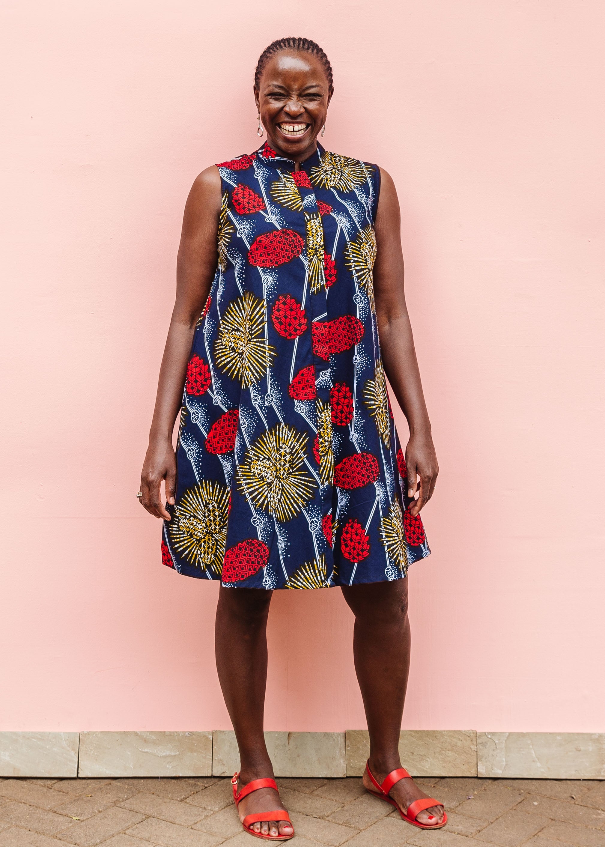 Model wearing navy sleeveless dress with red, yellow and white splatter print. 