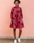 Model wearing red dress with floral vine print.